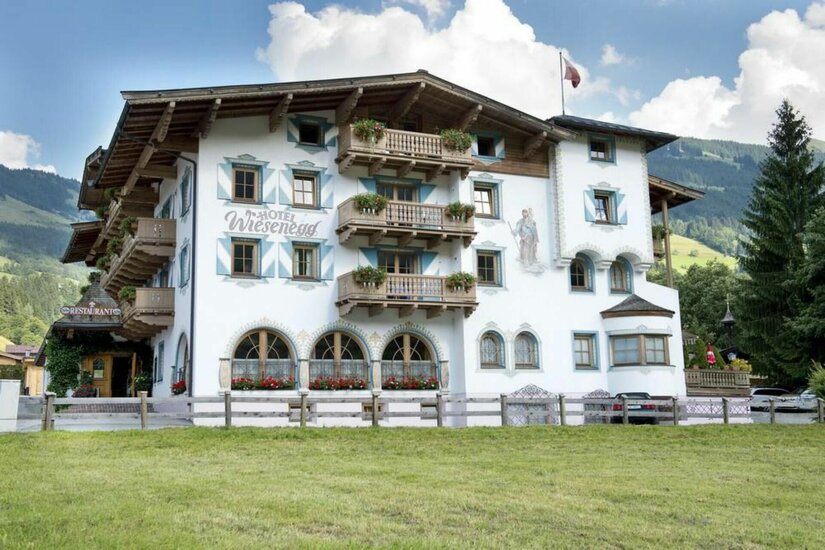 Hotel Wiesenegg im Sommer Vorderansicht des Hotel Wiesenegg mit Holzbalkonen und Wandmalereien vor einer Bergkulisse.