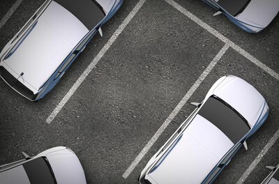 Draufsicht auf einen Asphaltparkplatz mit weißen Markierungen und geparkten Autos.