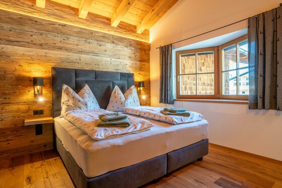 Schlafzimmer im Apartment Taxer Doppelbett in einem Schlafzimmer mit Altholzwänden und Holzbalkendecke.