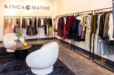 Kinga Mathe Store Kitzbühel Innenansicht eines Modegeschäfts mit Kleiderstangen voller Trachtenmode und zwei weißen Sesseln.