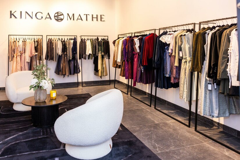 Kinga Mathe Store Kitzbühel Innenansicht eines Modegeschäfts mit Kleiderstangen voller Trachtenmode und zwei weißen Sesseln.