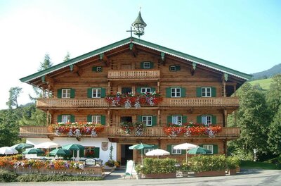 Traditionelles Holzgebäude mit Blumenbalkonen und einer Außenterrasse mit Sonnenschirmen.