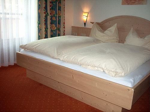 Doppelzimmer im Haus Mitterer Doppelbett aus hellem Holz in einem Hotelzimmer mit rotem Teppichboden.
