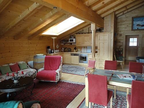 Wohnbereich Appartment Ölberg Wohn- und Essbereich in einer Holzhütte mit Dachschräge, Küchenzeile und roten Polstermöbeln.