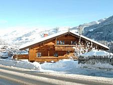 Haus Scherler im Winter Ein zweistöckiges Holzhaus mit schneebedecktem Dach vor einer winterlichen Bergkulisse.