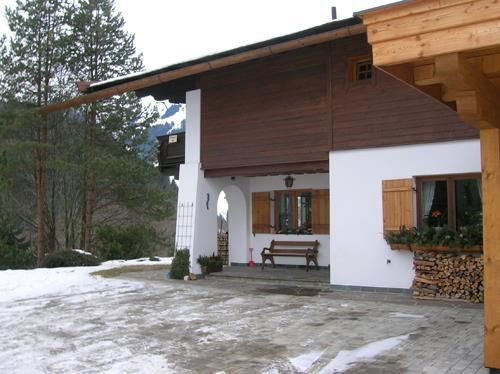 Außenansicht Haus Filzer im Winter Alpines Wohnhaus mit weißer Fassade, Holzverkleidung und einer Bank vor dem Eingang im Schnee.