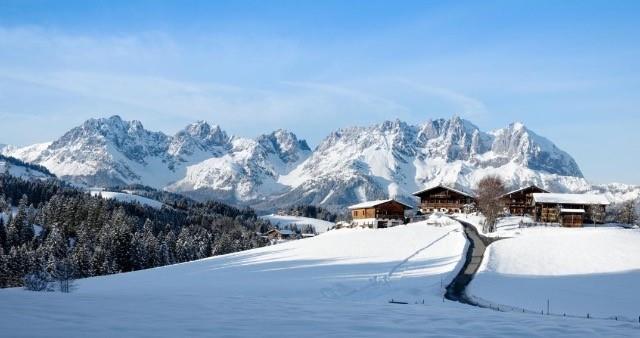 Hof Hintererb im Winter Verschneite Almhütten vor einem massiven, schneebedeckten Gebirgszug unter blauem Himmel.