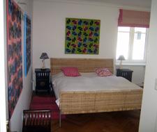 Schlafzimmer im Orsini-Rosenberg Schlafzimmer mit Doppelbett aus Korbgeflecht, Nachttischen und bunten Wandbildern.