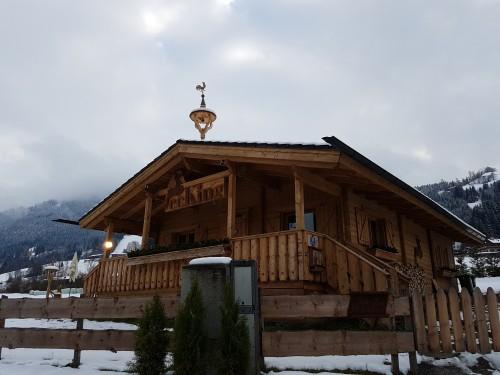 Cafe Ecking im Winter Holzhütte mit Terrasse und Wetterhahn vor verschneiten Bergen unter bewölktem Himmel.