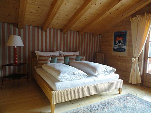 Schlafzimmer Appartment Ölberg Doppelbett in einem Zimmer mit Holzdecke, gestreifter Tapete und Nachttischlampe.