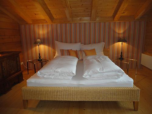 Schlafzimmer im Appartment Ölberg Doppelbett in einem Zimmer mit Holzdecke, gestreifter Tapete und zwei Nachttischlampen.