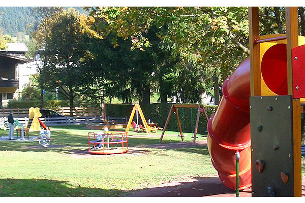 Kinderspielplatz mit roter Röhrenrutsche, Karussell und Schaukeln auf einer Rasenfläche.