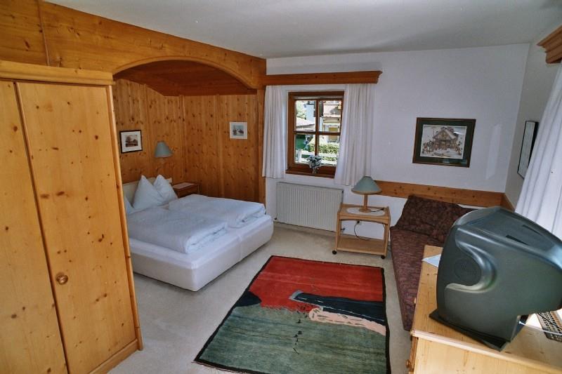 Zimmer im Ponapart GOLF & SCHI Schlafzimmer mit Doppelbett, Holzverkleidung, Kleiderschrank, Sofa und Fernseher.