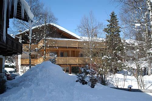 Haus Christophorus im Winter Mehrstöckiges Holzgebäude mit Balkonen in einer verschneiten Winterlandschaft unter blauem Himmel.