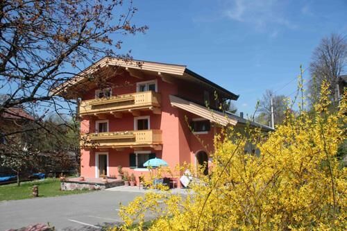 Gästehaus Sommer Senoner Dreistöckiges Gästehaus mit roter Fassade und Holzbalkonen hinter einem gelb blühenden Strauch.