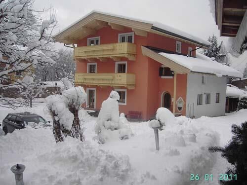 Gästehaus Senoner im Winter Ein mehrstöckiges, orangefarbenes Gästehaus mit Holzbalkonen in einer tief verschneiten Winterlandschaft.