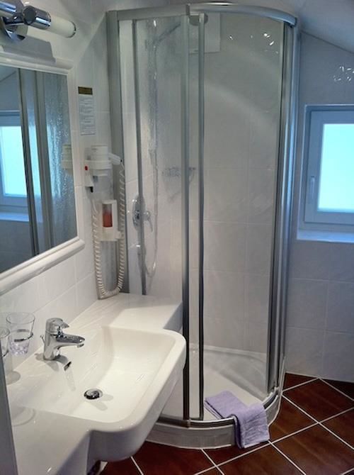 Bad Zimmer 6 Badezimmer mit weißem Waschbecken, Spiegel und einer Runddusche mit Glaskabine.